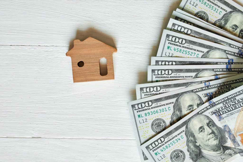 Small Wooden House And Hundred Dollar On White Background